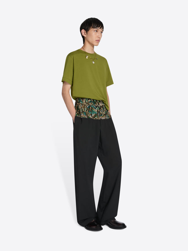 Person wearing a green top and black pants with a floral pattern on a white background