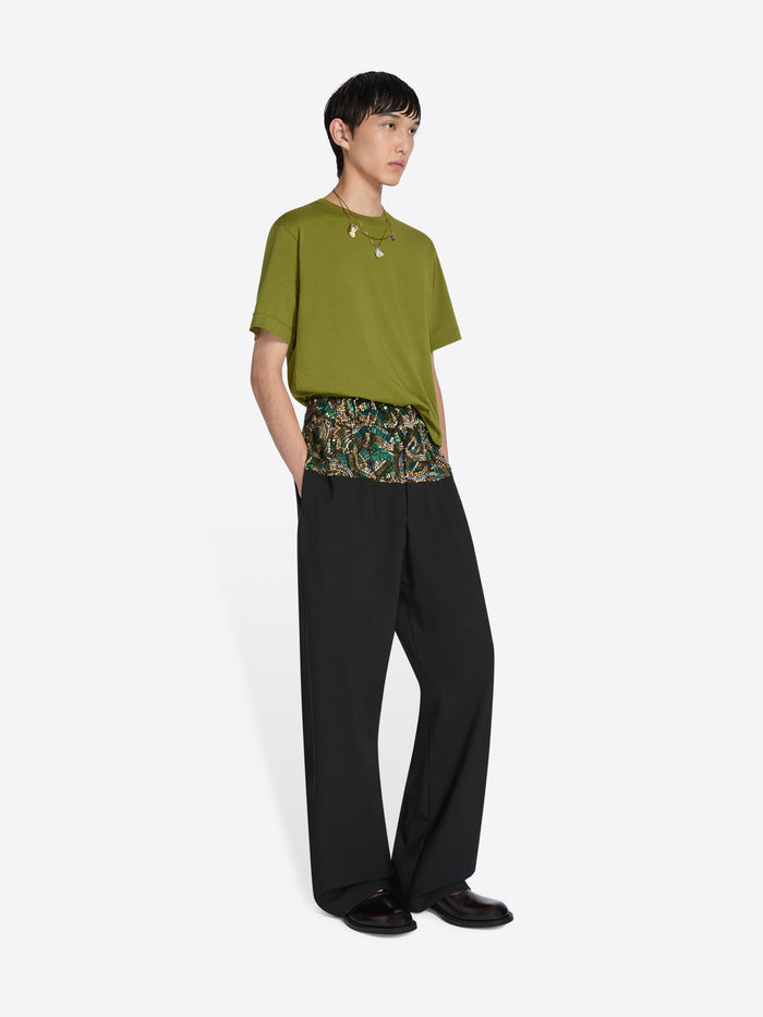 Person wearing a green top and black pants with a floral pattern on a white background