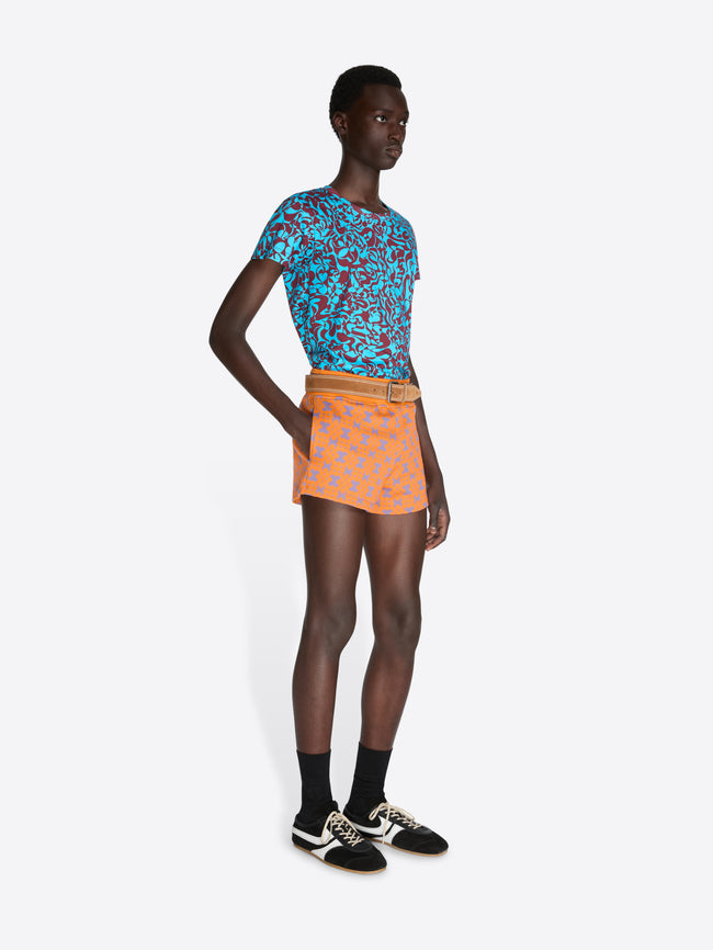 Model wearing a blue patterned top and orange skirt on a white background