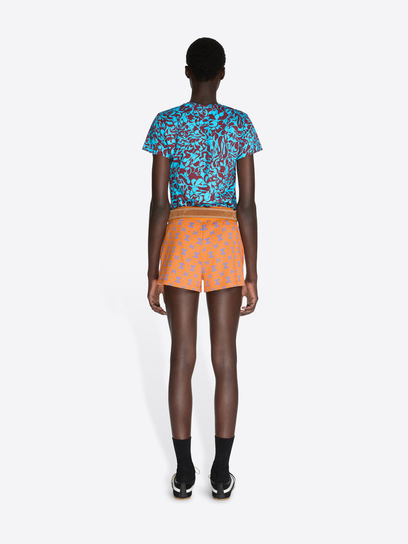 Person wearing a colorful patterned top and orange shorts on a white background