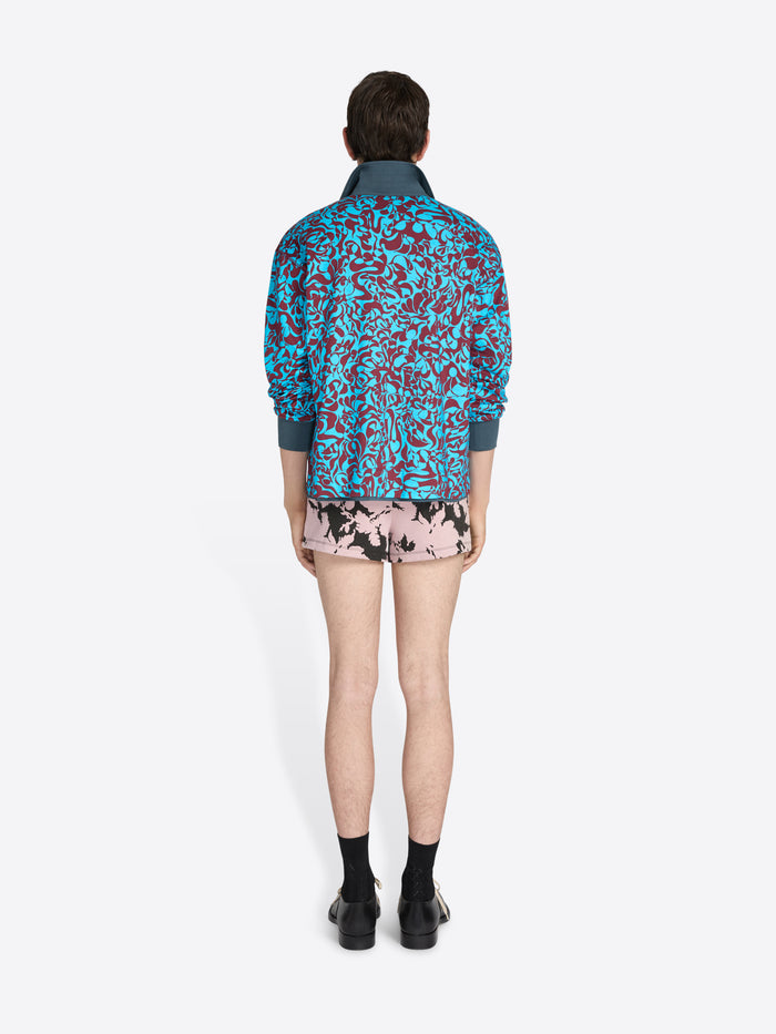 Person wearing a blue floral jacket and pink shorts on a white background