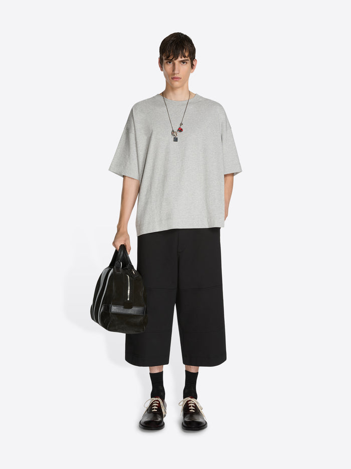 Person wearing a light gray t-shirt, black pants, and holding a black bag on a white background