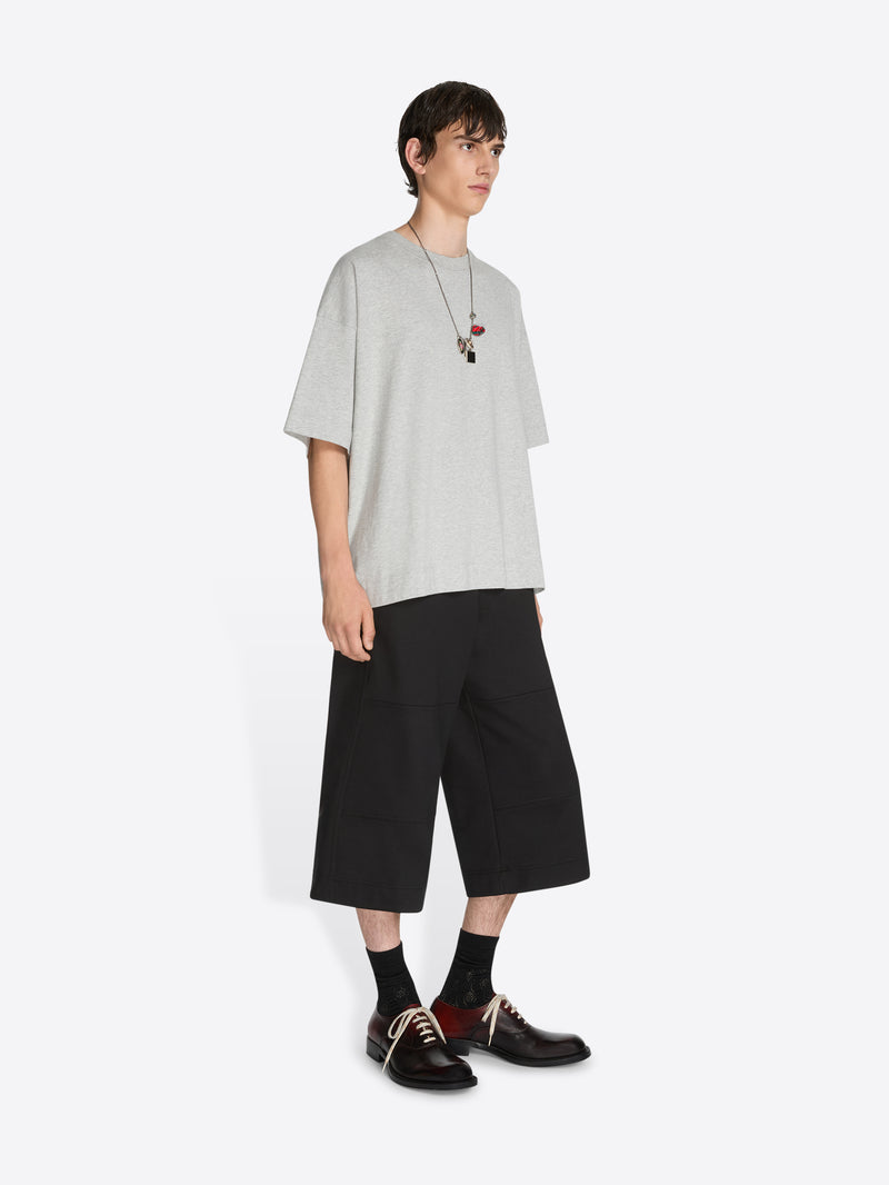 Person wearing a light gray oversized t-shirt, black shorts, and black shoes on a white background