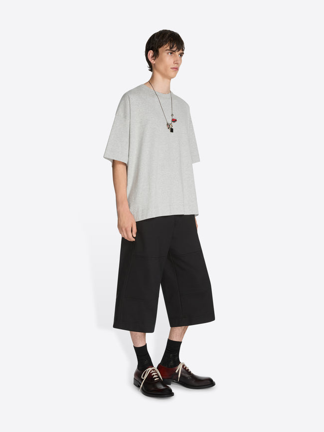 Person wearing a light gray oversized t-shirt, black shorts, and black shoes on a white background