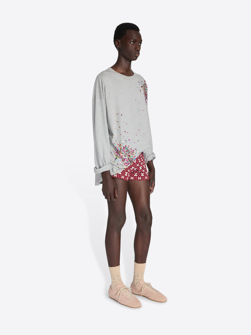 Person wearing a light gray sweatshirt with floral design and red shorts on a white background - Dries Van Noten