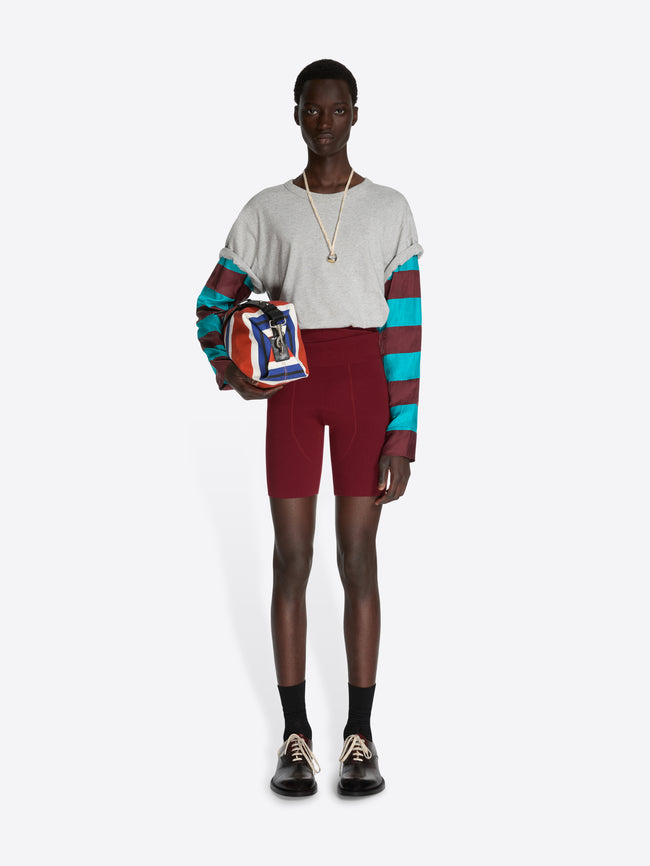 Person wearing a colorful sweater and red shorts holding a patterned bag on a white background