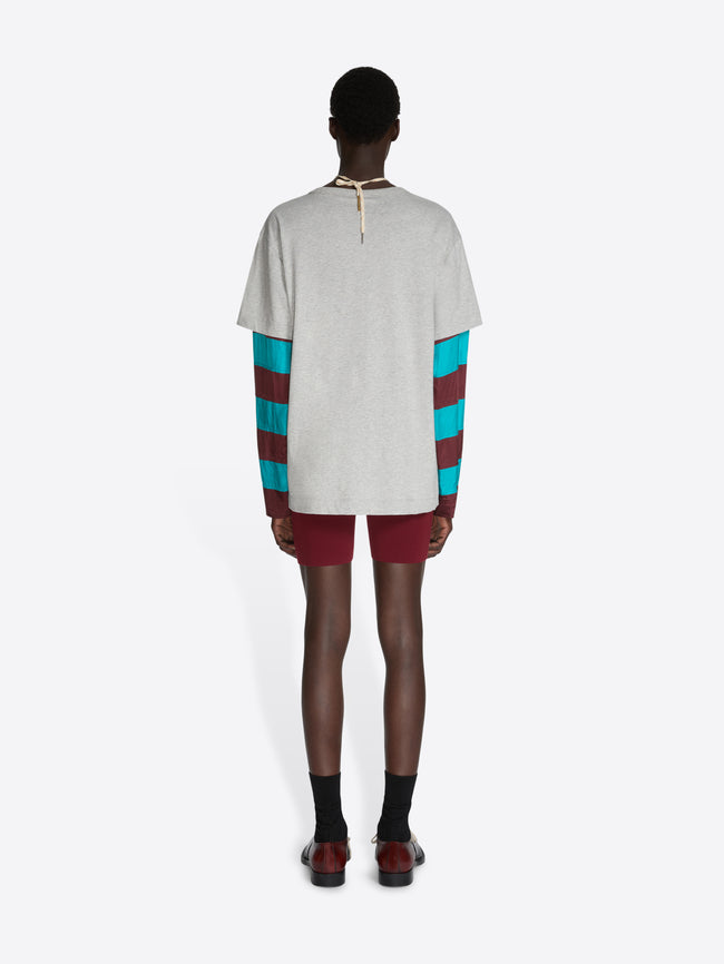 Person wearing a white t-shirt with colorful sleeves and maroon shorts on a white background