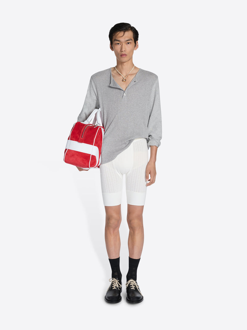 Person wearing a gray shirt, white shorts, black shoes, and holding a red and white bag on a white background - Dries Van Noten