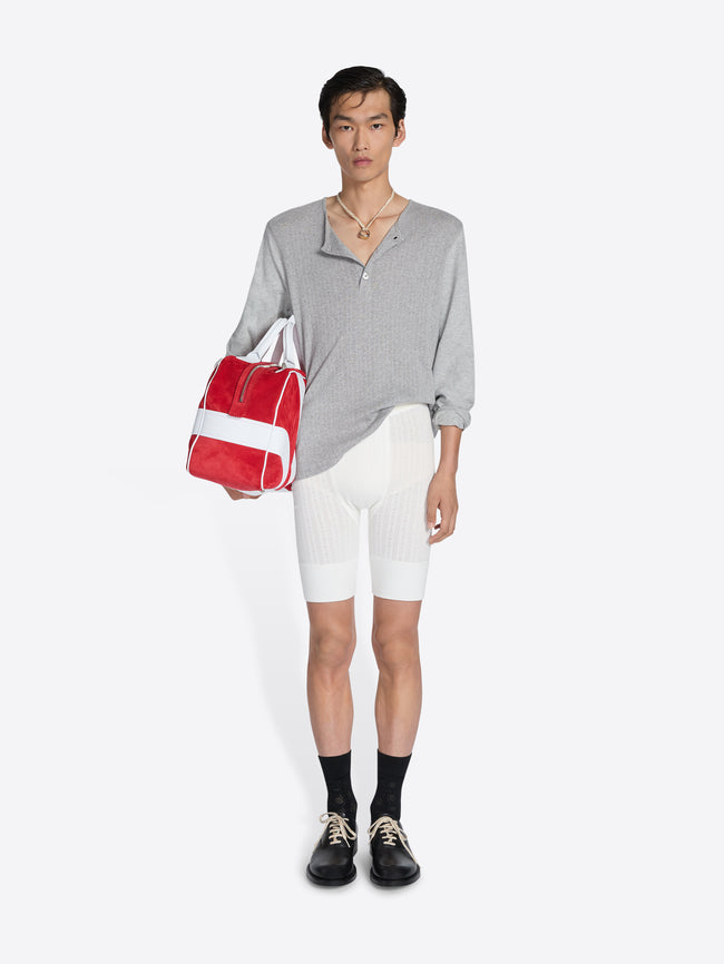 Person wearing a gray shirt, white shorts, black shoes, and holding a red and white bag on a white background - Dries Van Noten