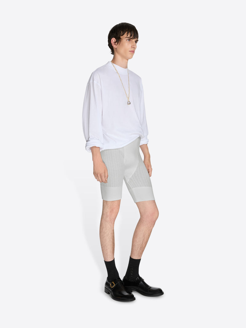 Person wearing a white shirt and light gray shorts on a white background - Dries Van Noten