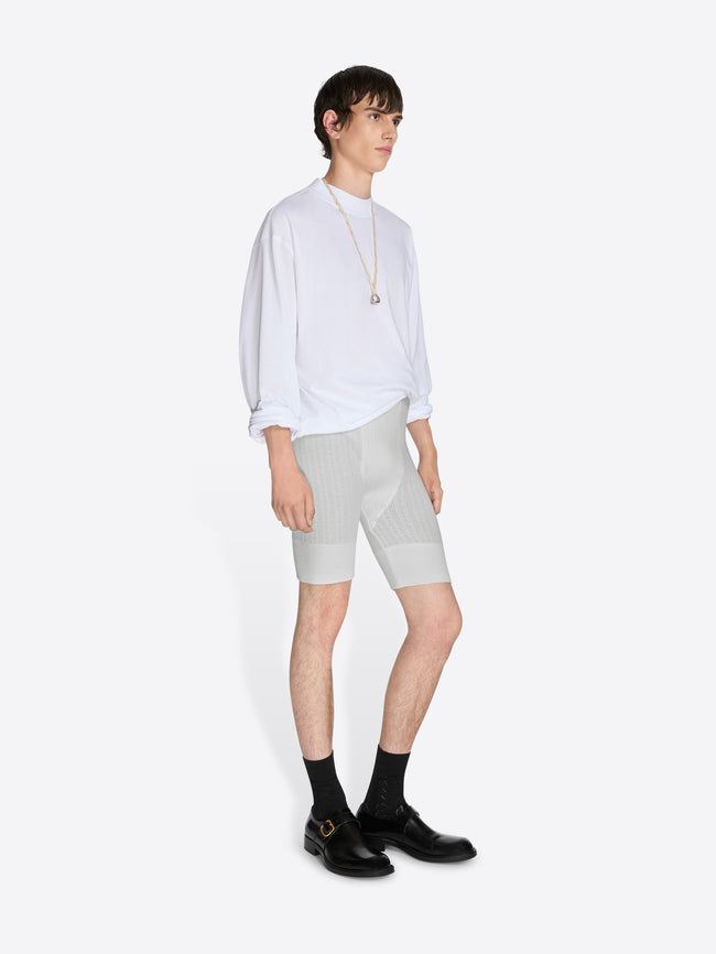 Person wearing a white shirt and light gray shorts on a white background - Dries Van Noten
