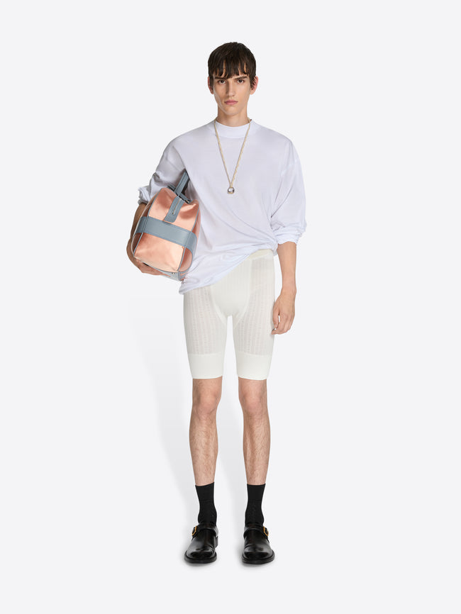 Person wearing a light gray shirt, white shorts, black shoes, and holding a pink bag on a white background - Dries Van Noten