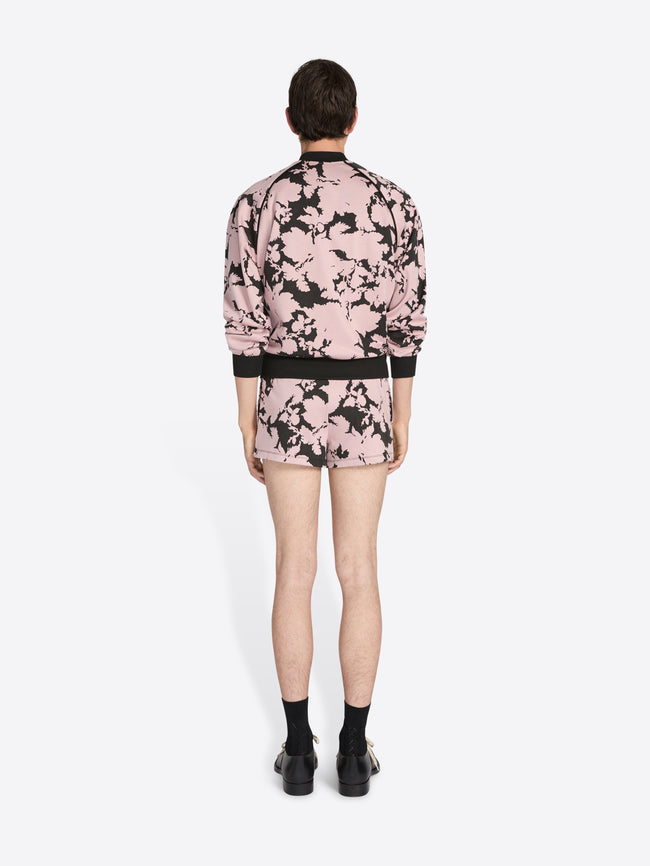 Person wearing a pink floral bomber jacket and shorts on a white background