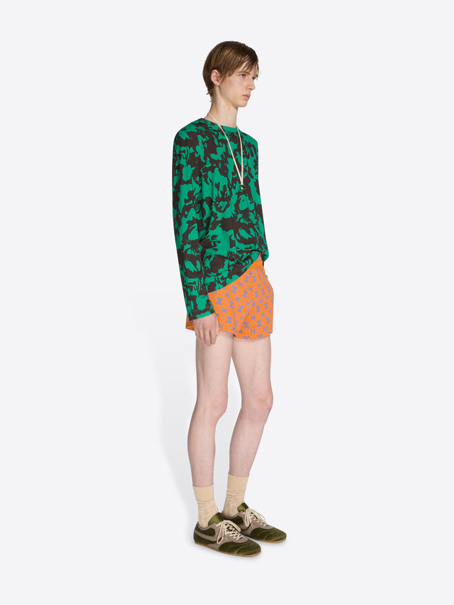 Person wearing a green patterned shirt and orange shorts on a white background