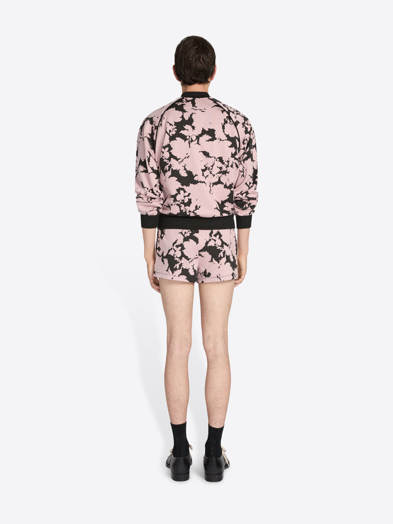 Person wearing a pink floral bomber jacket and shorts on a white background