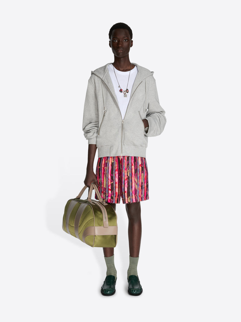 Person wearing a gray hoodie and colorful skirt, holding a green bag on a white background