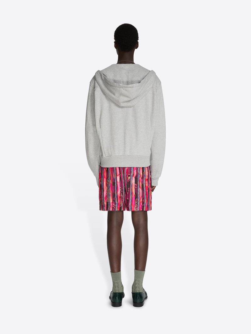Person wearing a gray hoodie and patterned shorts on a white background