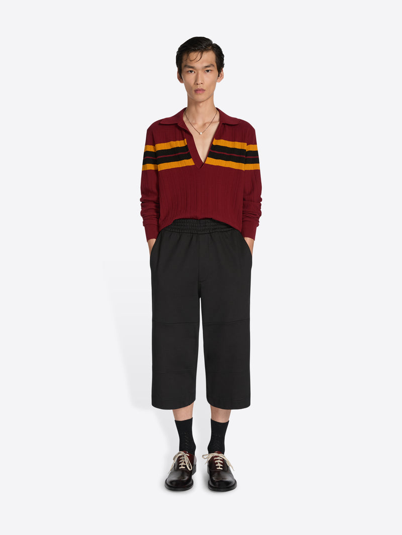 Person wearing a burgundy sweater with yellow and black stripes and black pants on a white background