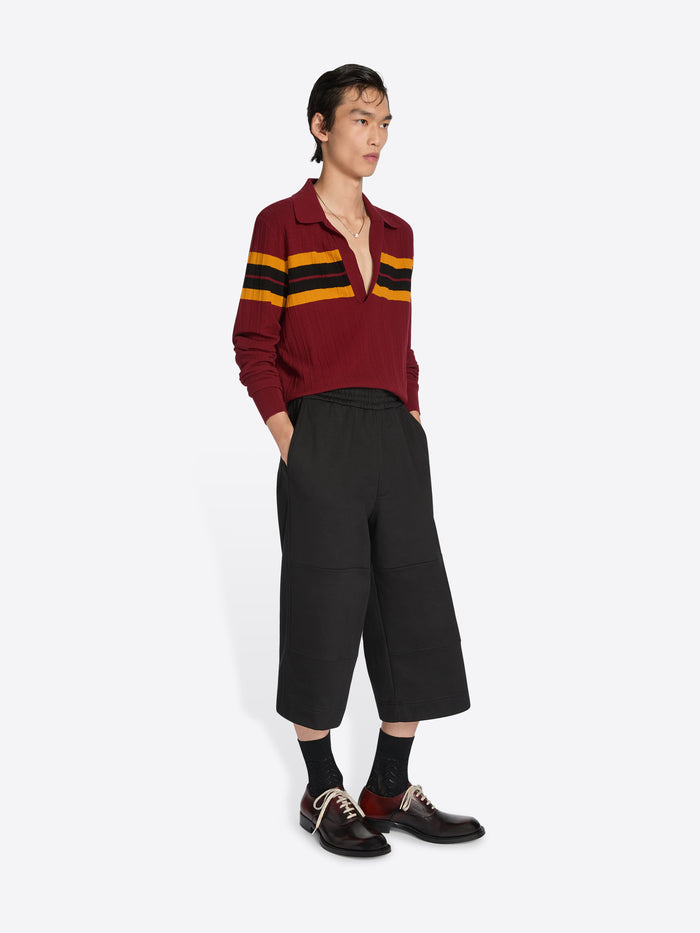 Person wearing a burgundy sweater with yellow stripes and black pants on a white background