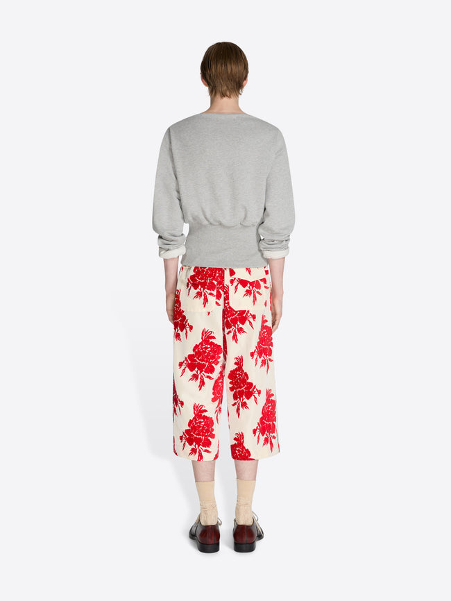 Person wearing a gray sweater and red floral pants on a white background