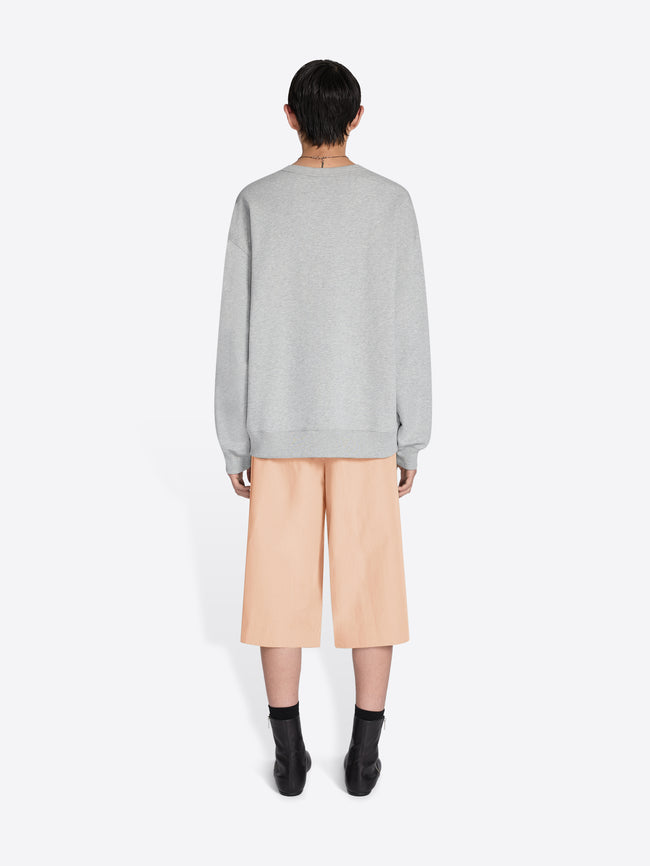 Person wearing a gray sweater and beige pants on a white background