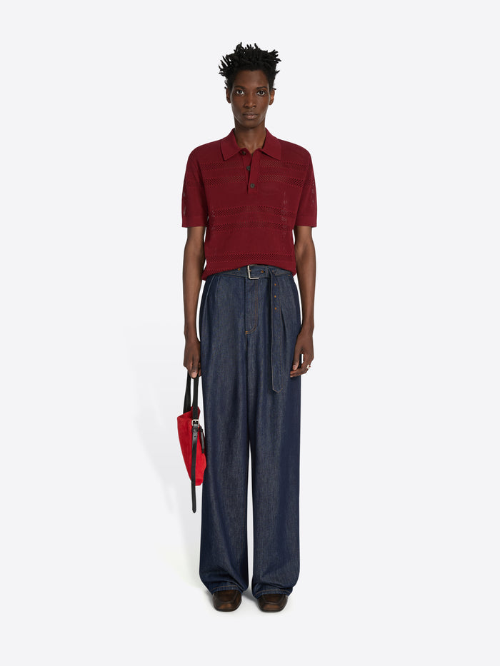 Person wearing a red polo shirt and blue wide-leg pants holding a red bag on a white background