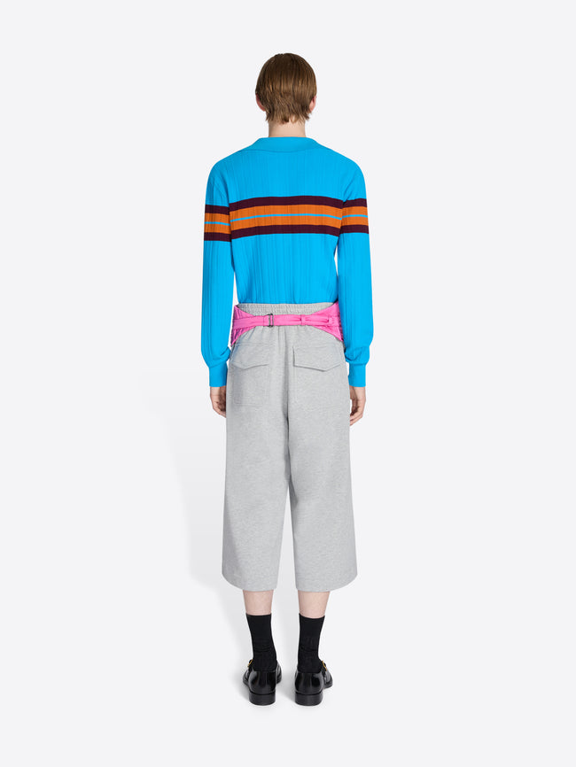 Person wearing a blue sweater with colorful stripes and gray pants on a white background - Dries Van Noten