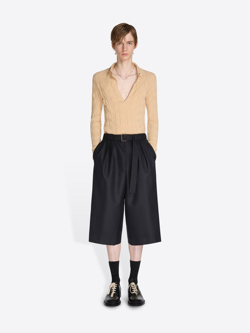 Person wearing a beige sweater and black pants on a white background - Dries Van Noten