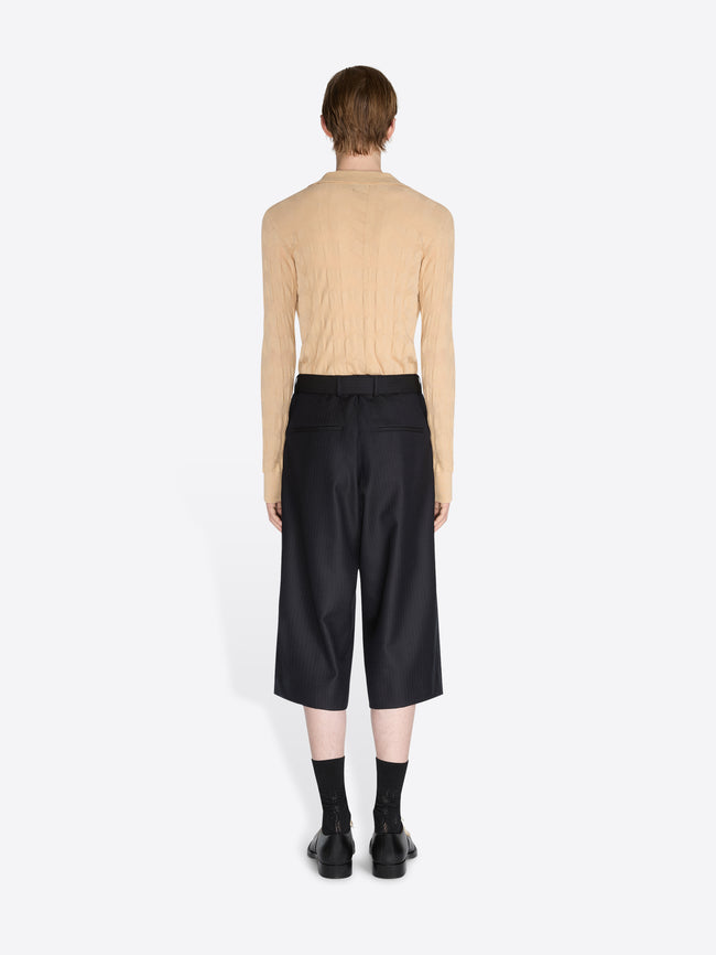 Person wearing a beige sweater and black pants on a white background - Dries Van Noten