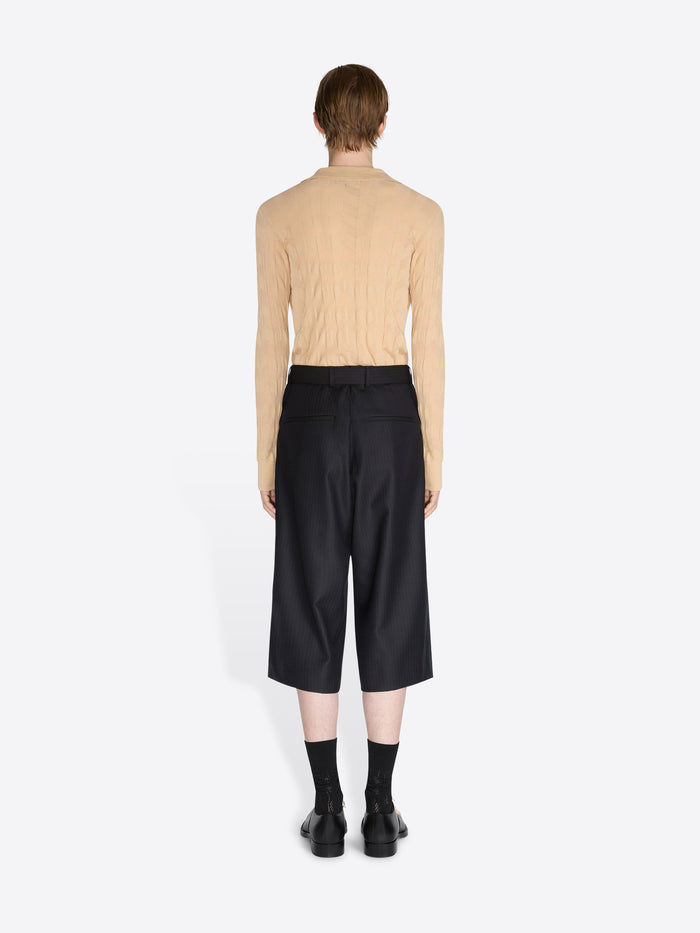 Person wearing a beige sweater and black pants on a white background - Dries Van Noten