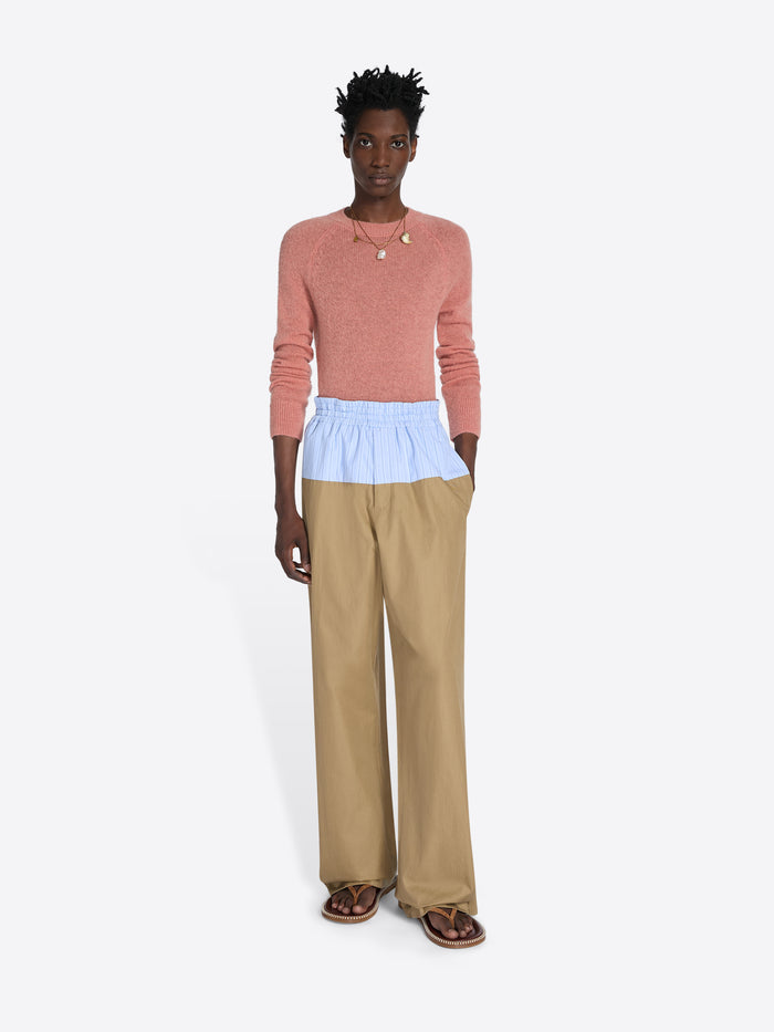 Person wearing a pink sweater, light blue top, and beige pants on a white background