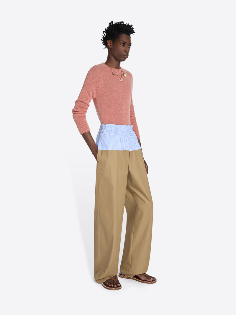 Person wearing a pink sweater, light blue top, and beige pants on a white background