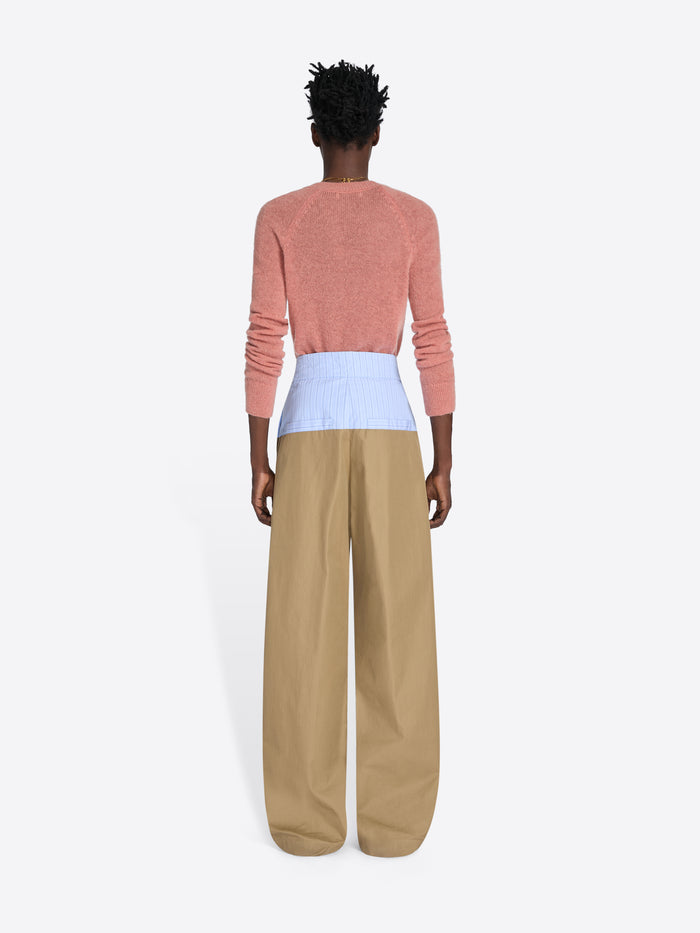 Person wearing a pink sweater and beige pants on a white background