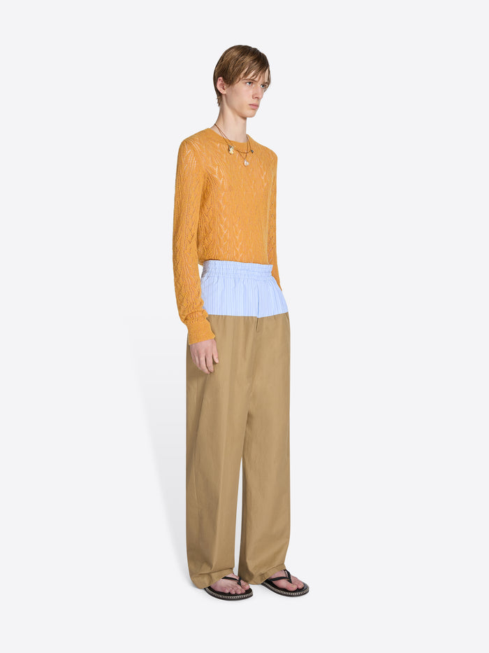 Person wearing a mustard yellow top and beige pants on a white background