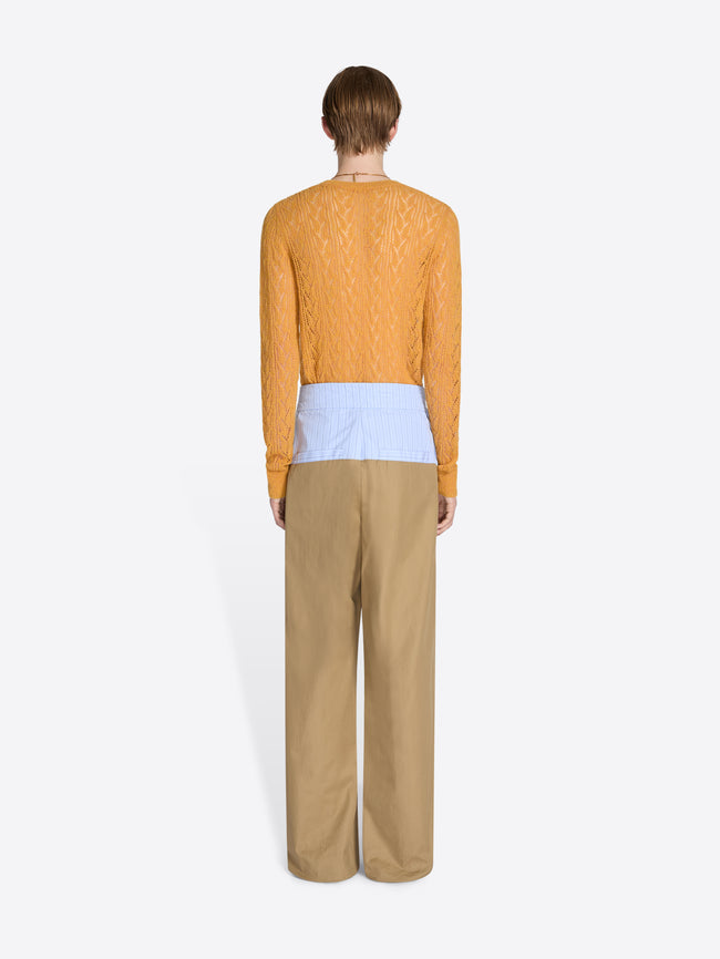Person wearing a mustard yellow sweater and beige pants on a white background