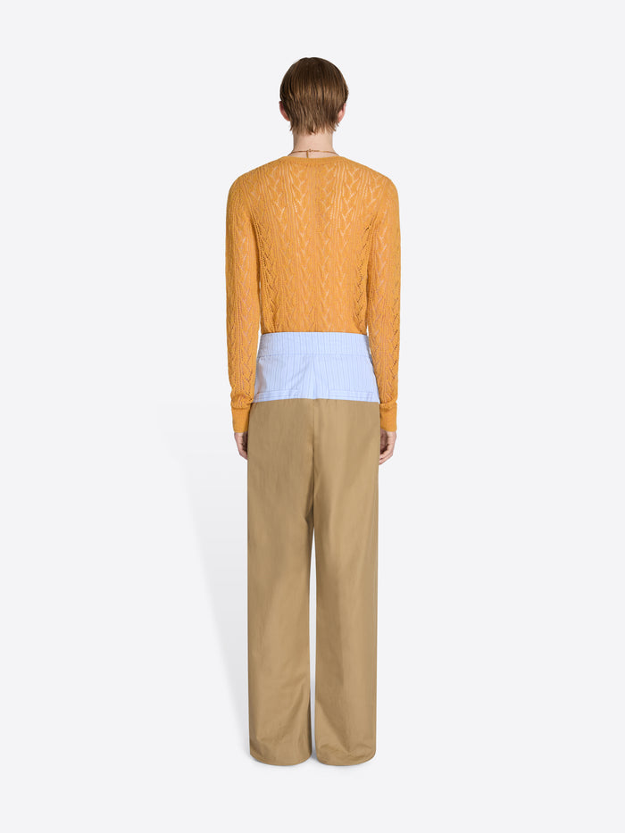 Person wearing a mustard yellow sweater and beige pants on a white background