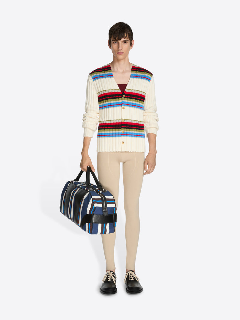 Person wearing a colorful striped sweater holding a striped bag on a white background