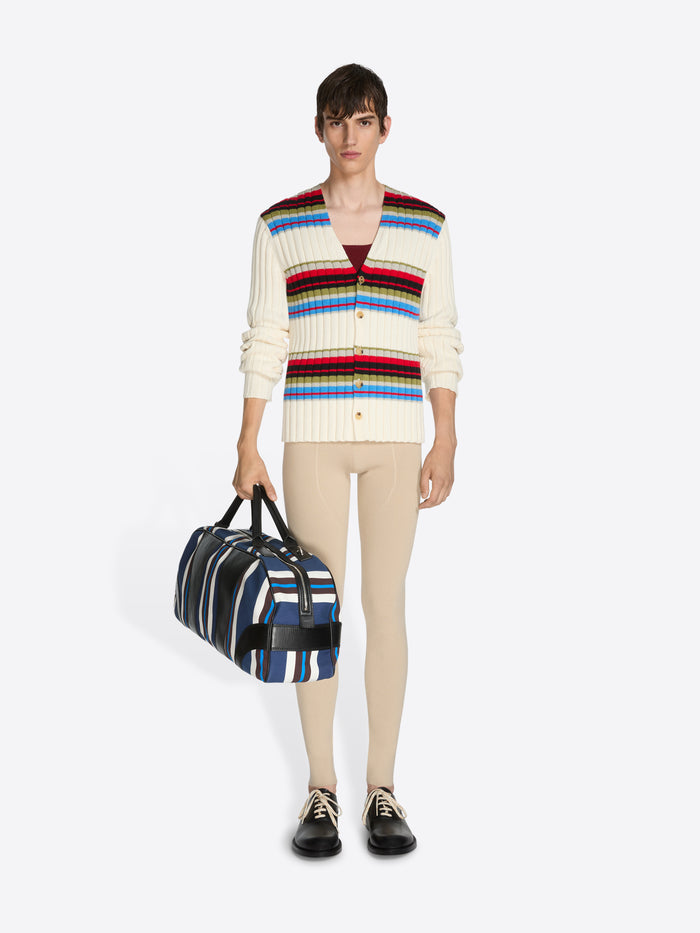 Person wearing a colorful striped sweater holding a striped bag on a white background
