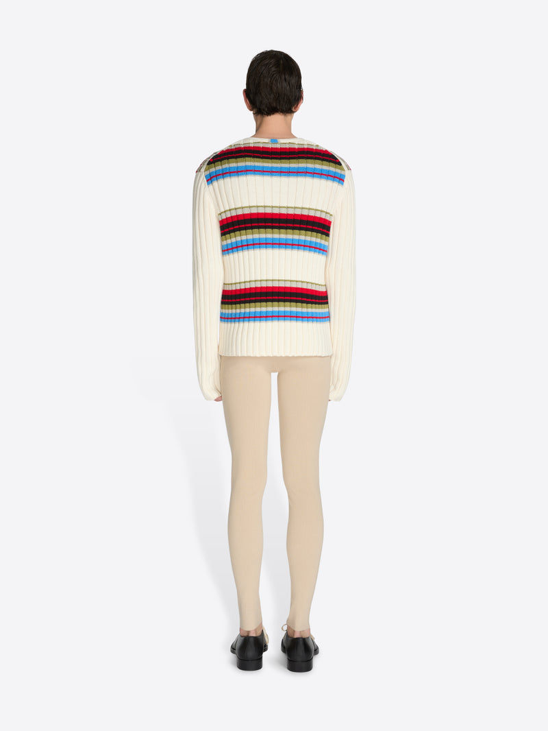 Person wearing a colorful striped sweater and beige pants on a white background