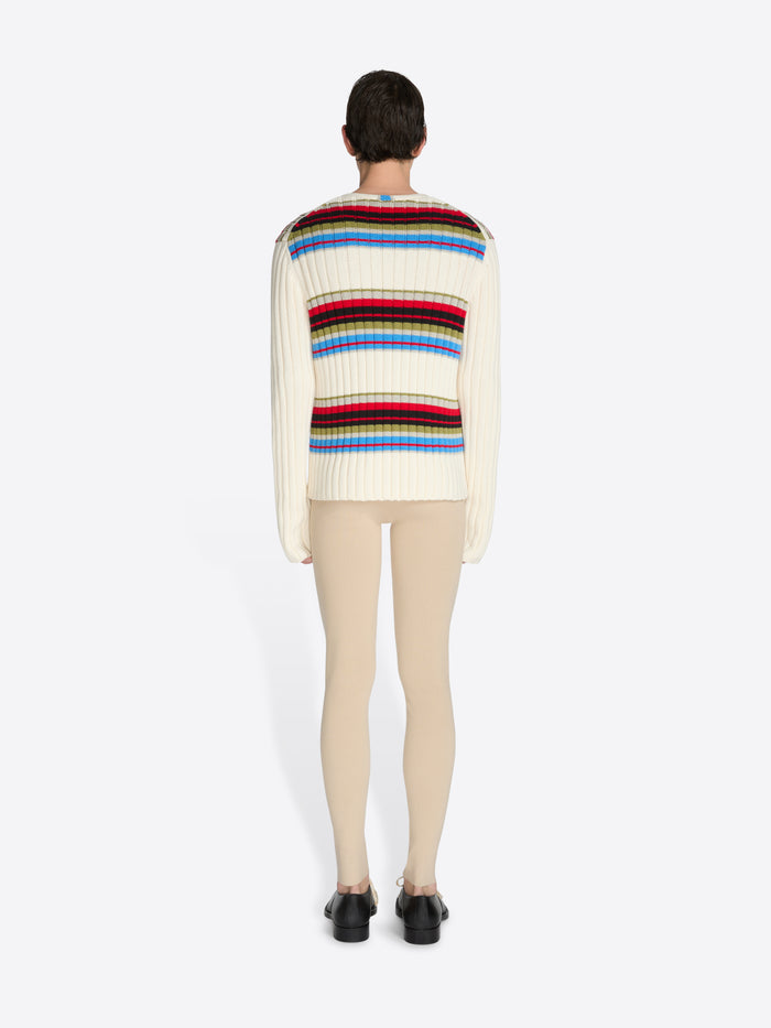 Person wearing a colorful striped sweater and beige pants on a white background