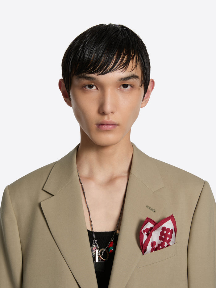 Man wearing a beige blazer with a red pocket square on a white background