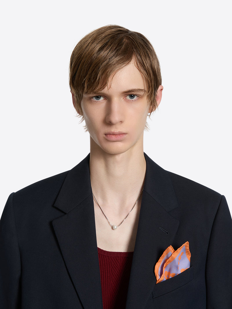 Person wearing a dark suit with an orange pocket square on a white background