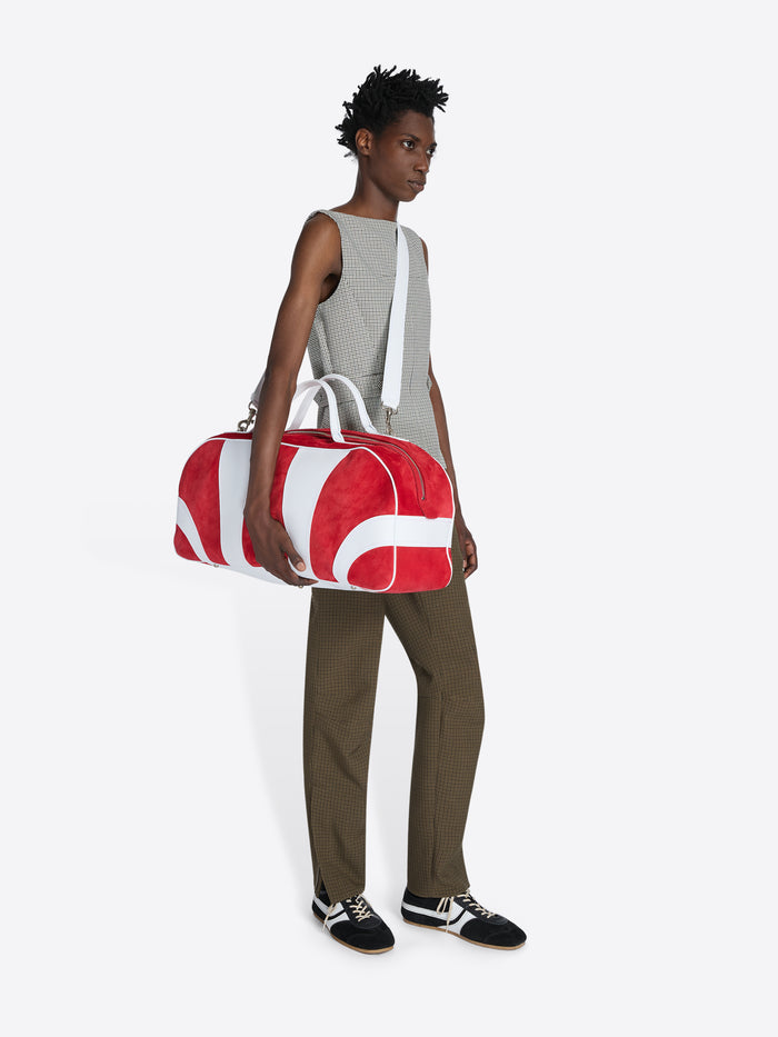 Person holding a red and white duffel bag on a plain background - Dries Van Noten