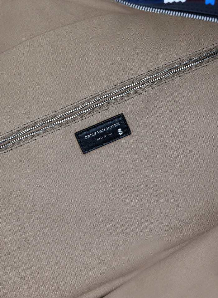 Close-up of a beige bag with a brand label on a blurred background - Dries Van Noten