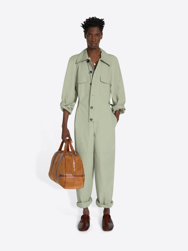 Person wearing a light green jumpsuit holding a brown leather bag on a white background - Dries Van Noten