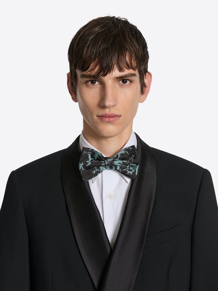 Man wearing a black tuxedo with a patterned bow tie on a white background