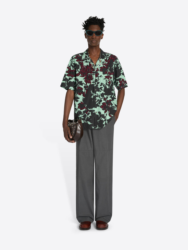 Person wearing a patterned shirt and gray pants on a white background