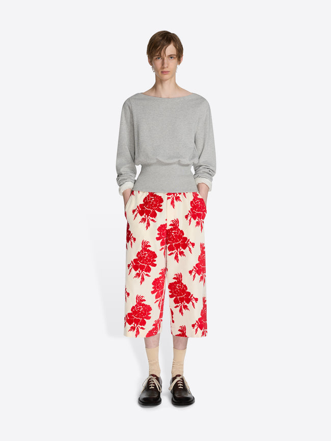 Person wearing a gray sweater and red floral pants on a white background