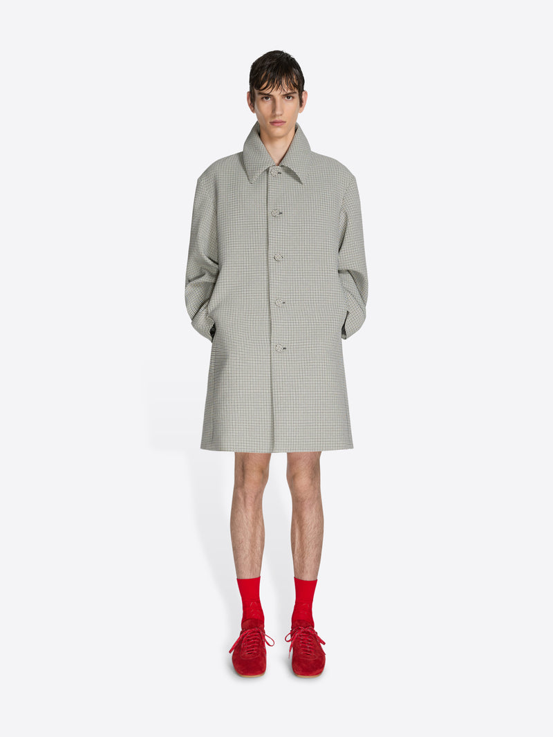 Person wearing a light gray checkered coat with red shoes on a white background