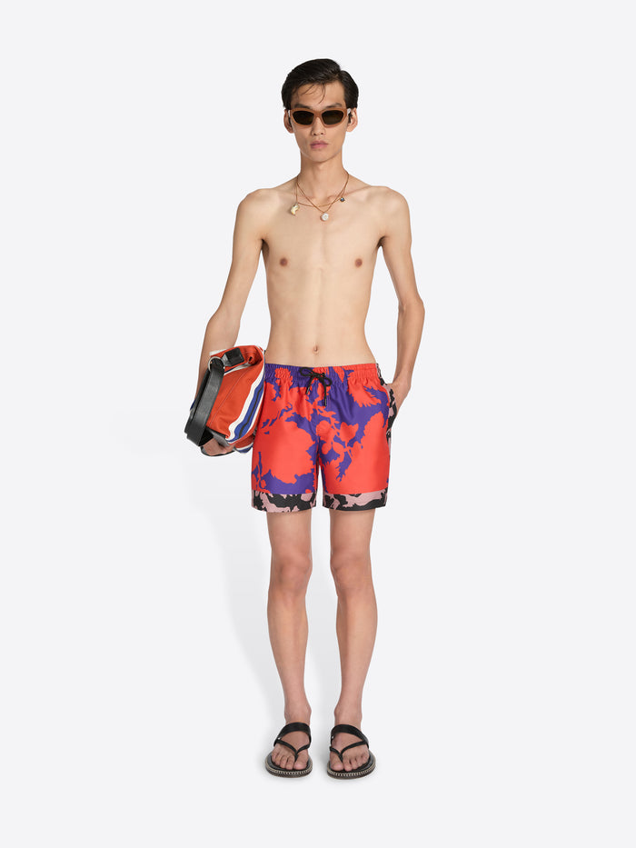 Man wearing colorful swim shorts holding a bag on a white background